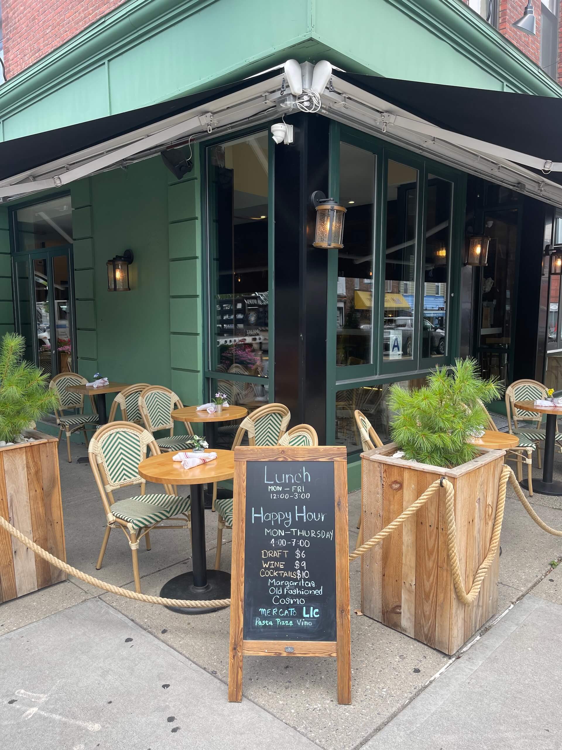 Sidewalk tables and a chalkboard sign with the lunch and happy hour menu